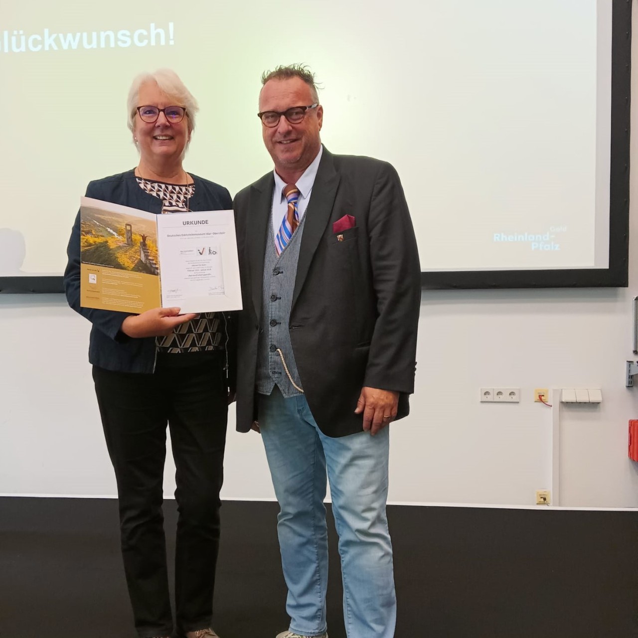 Frau Anette Fuhr hält die Urkunde für die Zertifizierung der Barrierefreiheit in den Händen, direkt daneben steht Staatssekretär Andy Becht