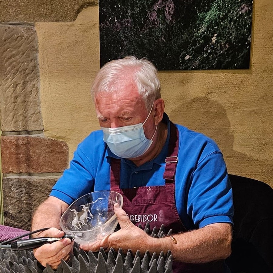 Der Graveur Uli Pauly hält eine Bergkristall Schale in der Hand und graviert mit einem biegsamen Graveurwerkzeug ein Motiv