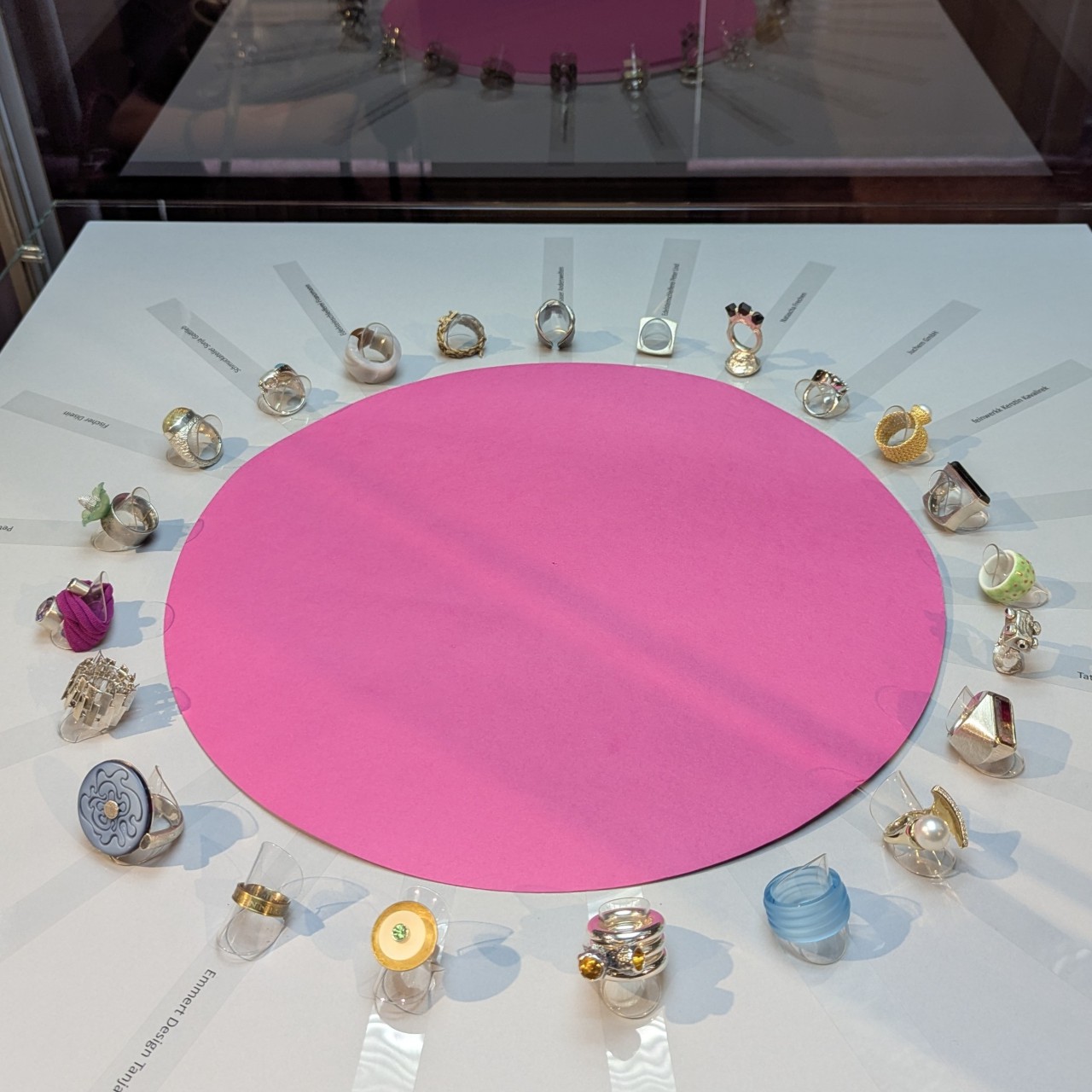 Gruppe von Unikat-Ringen aus verschiedenen Werkstätten kreisförmig um eine pinke Fläche angeordnet