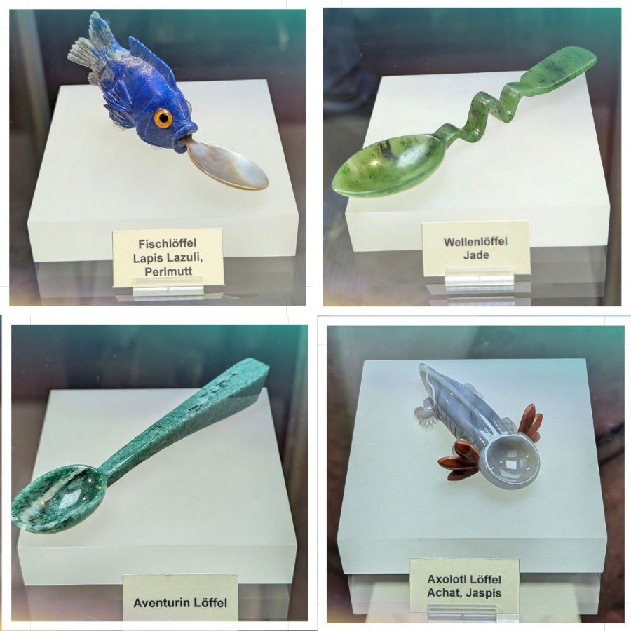 Vier kunstvoll gestaltete Löffel aus Edelsteinen, darunter ein Fischlöffel aus Lapislazuli und Perlmutt, ein wellenförmiger Löffel aus Jade, ein Aventurinlöffel und ein Axolotl Löffel aus Achat mit rotem Jaspis.