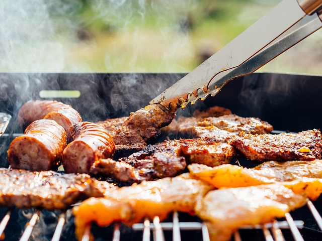 Man sieht einen Teil von einem Grillrost darauf Fleisch und Würstchen. Vom Rost steigt ein bisschen Rauch auf.